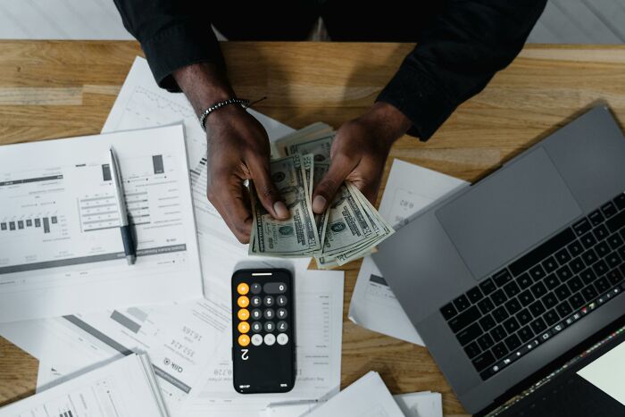 Person counting money over financial documents with a laptop and calculator, addressing common internet stereotypes.