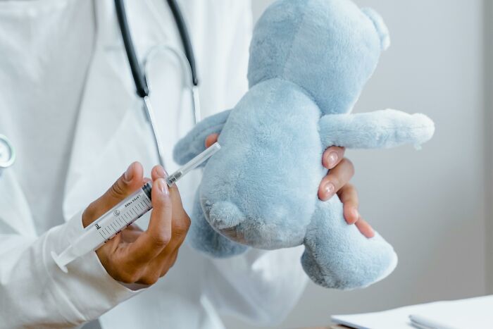Doctor playfully giving an injection to a teddy bear, challenging common stereotypes in a medical setting.