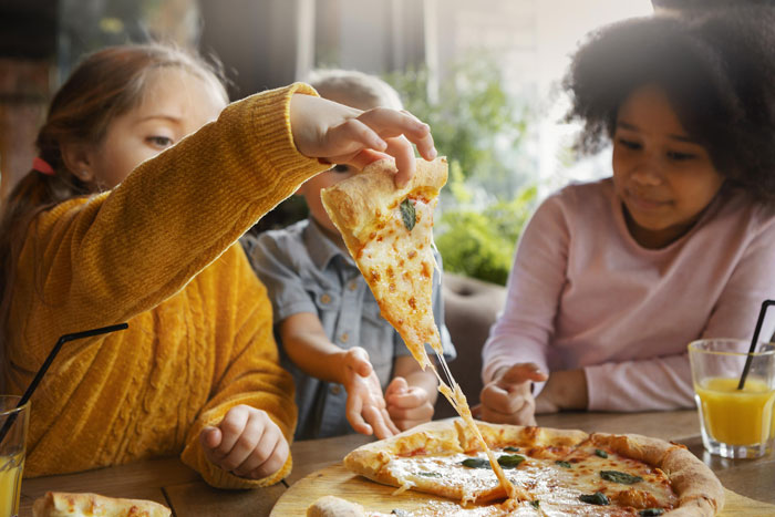 Children enjoying pizza at a restaurant, illustrating the issue of unruly kids affecting dining experiences. Children enjoying pizza at a restaurant, illustrating the issue of unruly kids affecting dining experiences.