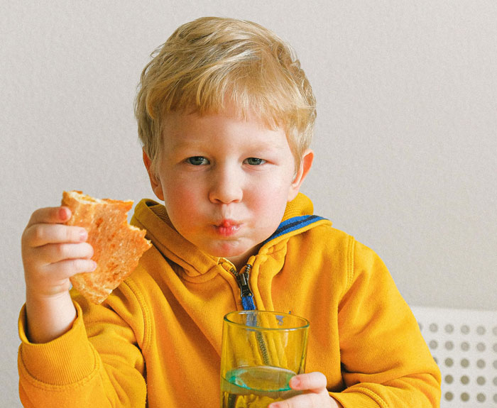 Child in yellow hoodie eating pizza, holding a glass, reflecting a pizza place's frustration with unruly kids. Child in yellow hoodie eating pizza, holding a glass, reflecting a pizza place's frustration with unruly kids.
