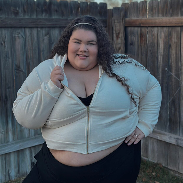 Plus-size woman confidently wearing a white hoodie in front of a wooden fence. Plus-size woman confidently wearing a white hoodie in front of a wooden fence.