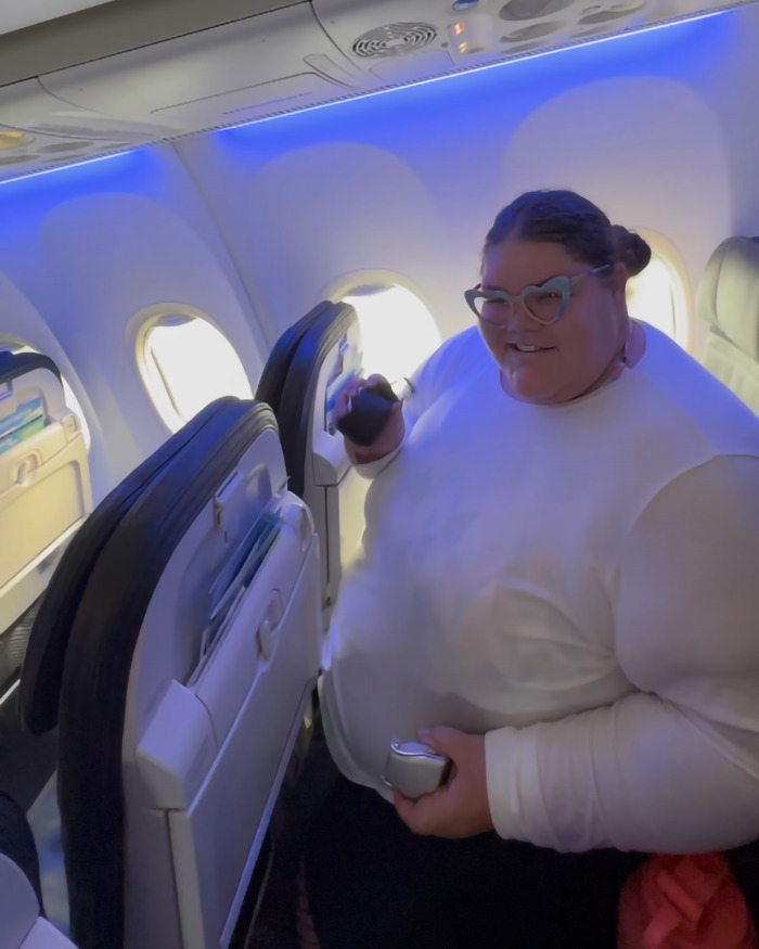 Plus-size woman in airplane seat, holding a phone, addressing airline seating policies. Plus-size woman in airplane seat, holding a phone, addressing airline seating policies.