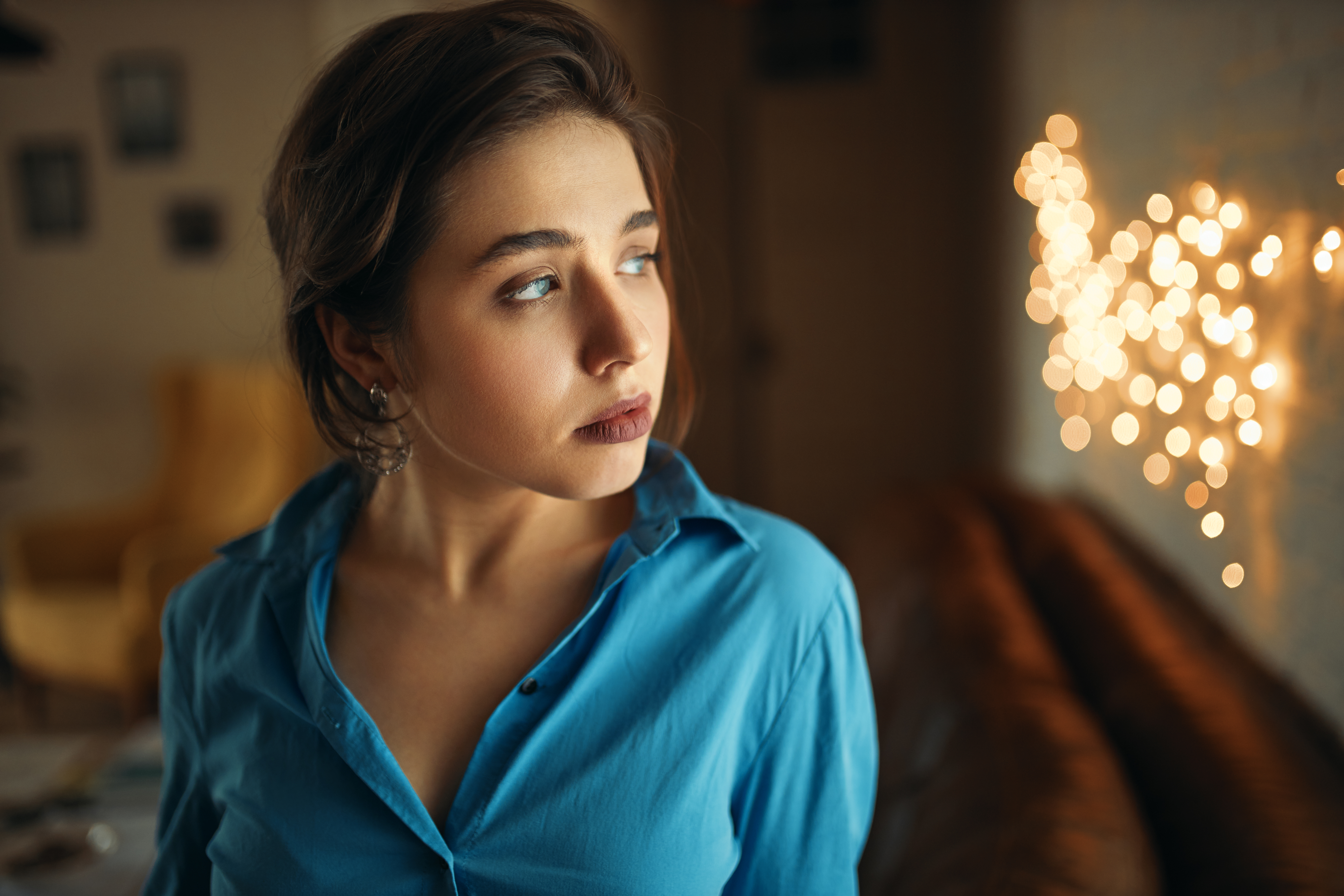 Woman in blue shirt looking away, pondering family holiday invitation issues indoors. Woman in blue shirt looking away, pondering family holiday invitation issues indoors.