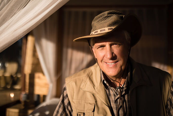 Man in outdoor gear with a hat smiling, sunlight highlighting his face, insignificant thing in nature background.