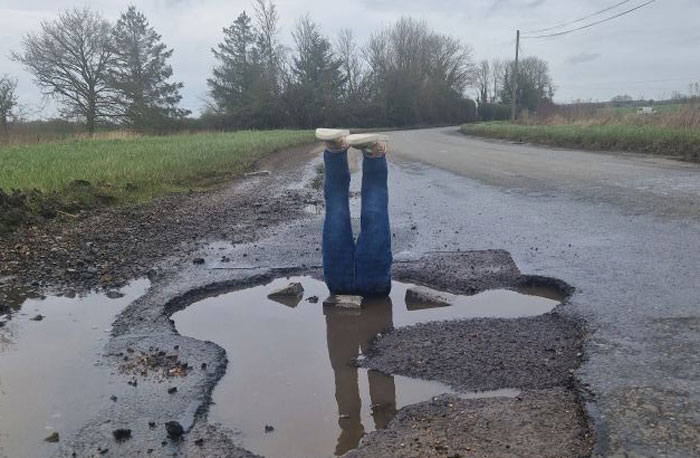 Legs sticking out of a pothole on a rural road; prank alerts officials to local hero’s concern. Legs sticking out of a pothole on a rural road; prank alerts officials to local hero’s concern.