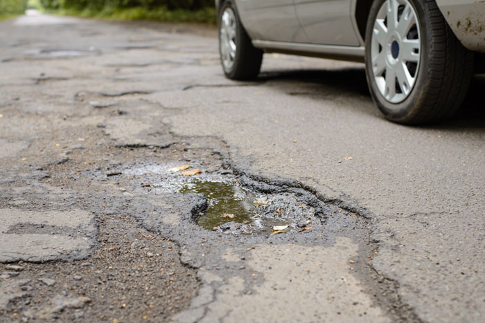 Pothole on a road with a car nearby, highlighting local hero's prank alerting officials. Pothole on a road with a car nearby, highlighting local hero's prank alerting officials.