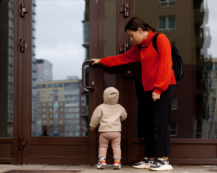 A woman in a red sweater and child at a door, relevant to pregnant-wife-childcare. A woman in a red sweater and child at a door, relevant to pregnant-wife-childcare.