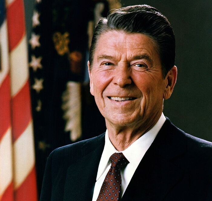 Smiling man in a suit with a U.S. flag in the background, representing themes of sneaky scams.