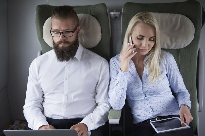 Man and woman in white shirts on a train; pretty privilege in everyday life as they use tech devices.