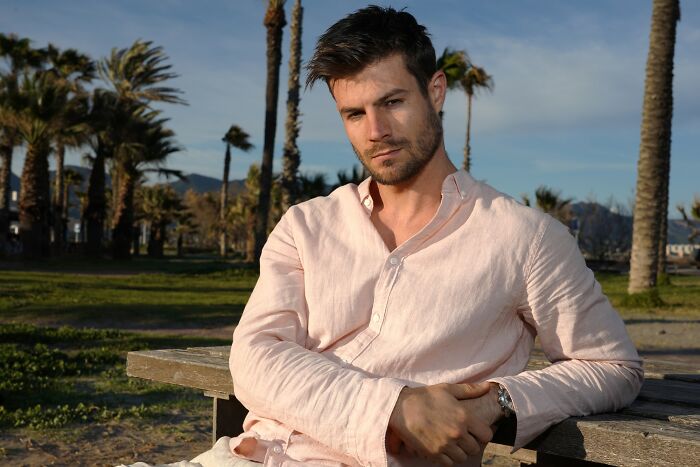 Man in a light shirt sitting outdoors on a bench, illustrating the effects of pretty privilege among men.