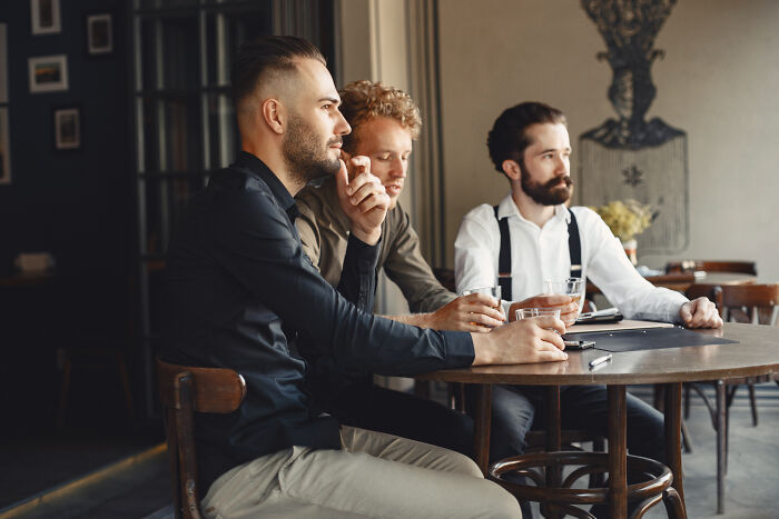 Three men sitting in a cafe, discussing while exemplifying pretty privilege in a relaxed, stylish setting.