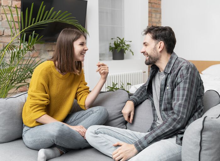 A man and woman smiling and talking on a couch, illustrating the concept of pretty privilege in social interactions.