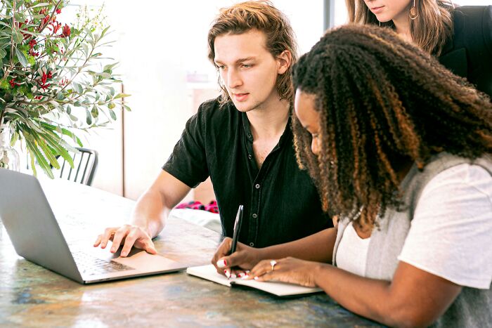 Man discussing project with colleagues, highlighting pretty privilege dynamics, as they work together at a table with a laptop.