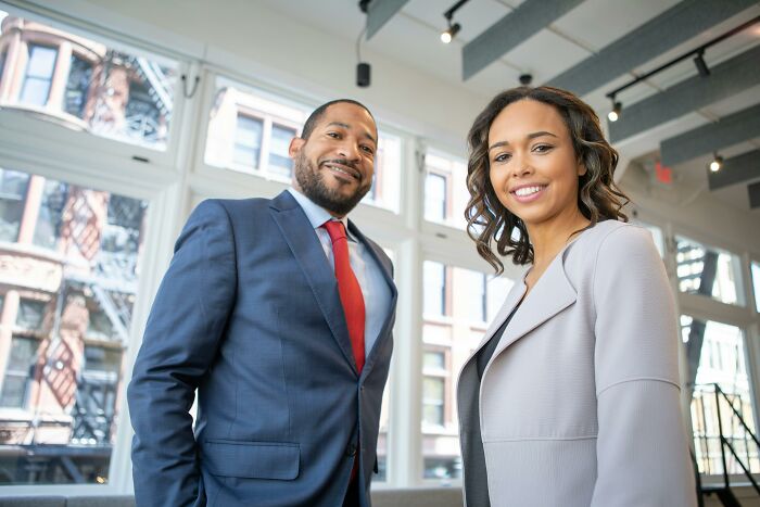 Man in suit and woman in business attire smiling indoors, illustrating pretty privilege in professional settings.