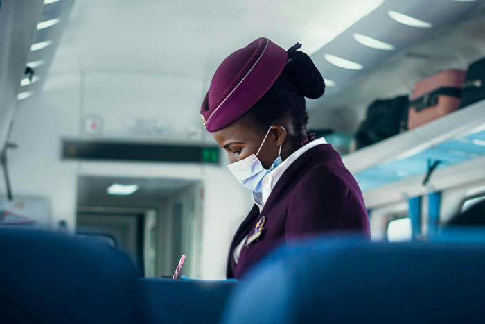 Airline attendant in uniform and mask onboard, checking documents mid-flight. Airline attendant in uniform and mask onboard, checking documents mid-flight.