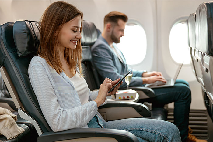 Airplane passengers seated, one using a phone, the other a laptop, highlighting seat choice options and comfort. Airplane passengers seated, one using a phone, the other a laptop, highlighting seat choice options and comfort.