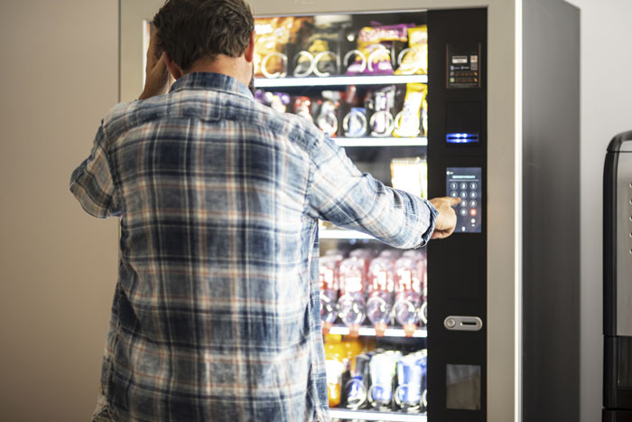 Man in a plaid shirt using a vending machine, reflecting themes of free rides and lending money. Man in a plaid shirt using a vending machine, reflecting themes of free rides and lending money.