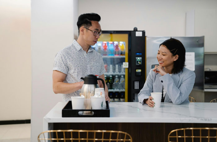 Two colleagues chatting casually over coffee in an office break room. Two colleagues chatting casually over coffee in an office break room.