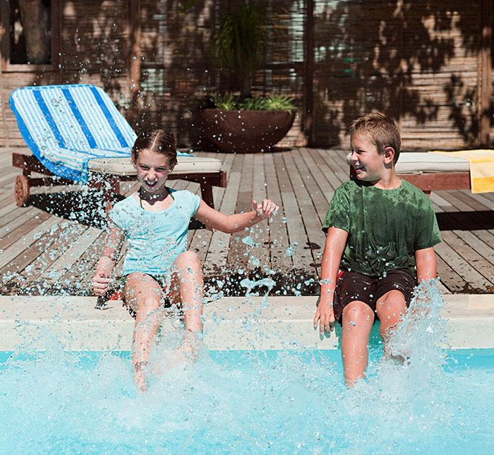 Kids splashing water at a pool, enjoying a sunny day while sitting at the edge. Kids splashing water at a pool, enjoying a sunny day while sitting at the edge.