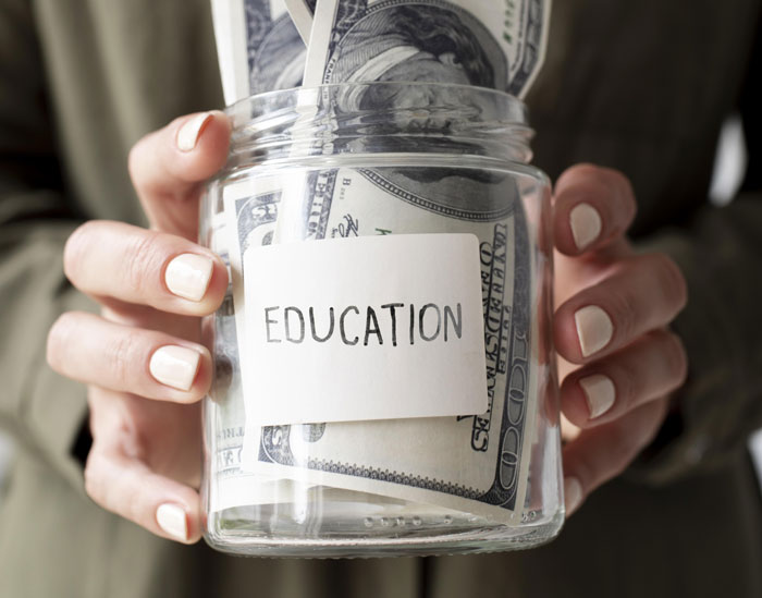 A jar labeled "Education" filled with cash, symbolizing financial burdens in paying for college. A jar labeled "Education" filled with cash, symbolizing financial burdens in paying for college.