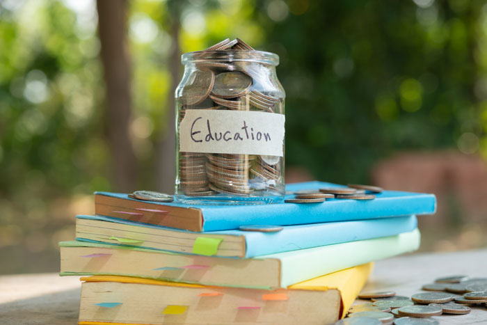 Jar labeled "Education" filled with coins on stacked books, illustrating a college fund concept. Jar labeled "Education" filled with coins on stacked books, illustrating a college fund concept.
