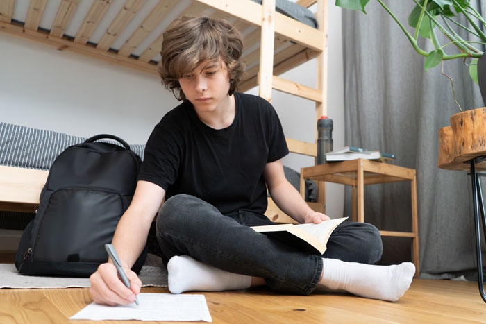 Teen boy studying on the floor in casual attire, highlighting family tension over college fund decisions. Teen boy studying on the floor in casual attire, highlighting family tension over college fund decisions.