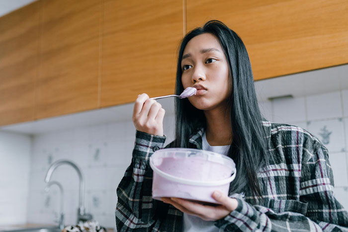 Young woman with a plaid shirt eating ice cream in a kitchen, tasting a surprise flavor. Young woman with a plaid shirt eating ice cream in a kitchen, tasting a surprise flavor.