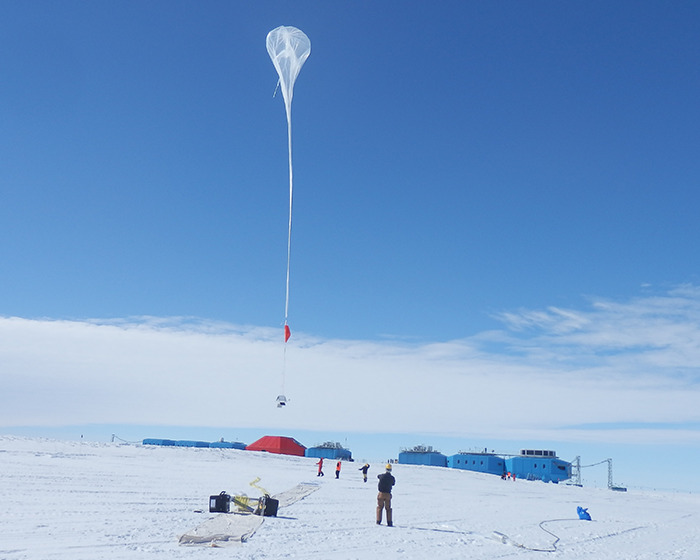 Balloon launch at remote Antarctica base against a clear blue sky, with scientists observing equipment on the snow. Balloon launch at remote Antarctica base against a clear blue sky, with scientists observing equipment on the snow.