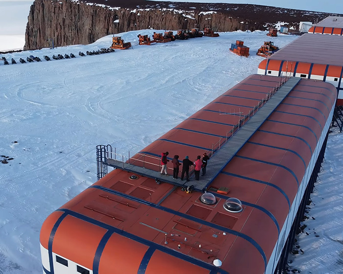 Remote Antarctica base with people on the roof, surrounded by snow and machinery, highlighting a desolate setting. Remote Antarctica base with people on the roof, surrounded by snow and machinery, highlighting a desolate setting.