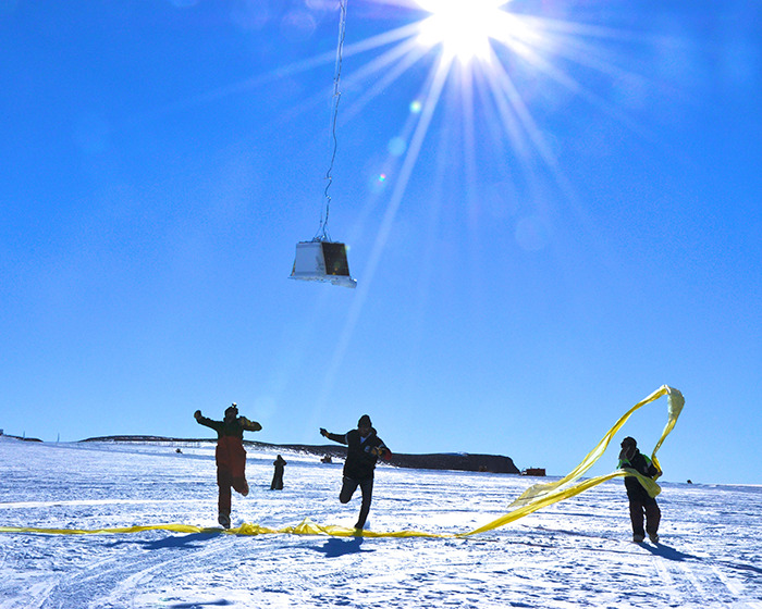 Scientists in Antarctica working under the sun with equipment suspended in the sky above them. Scientists in Antarctica working under the sun with equipment suspended in the sky above them.