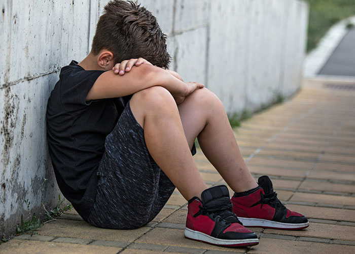 A young boy in red sneakers sits sadly against a wall, suggesting family discipline issues. A young boy in red sneakers sits sadly against a wall, suggesting family discipline issues.