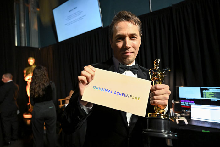 Winner holding Oscar 2025 for Original Screenplay, smiling backstage with award envelope. Winner holding Oscar 2025 for Original Screenplay, smiling backstage with award envelope.