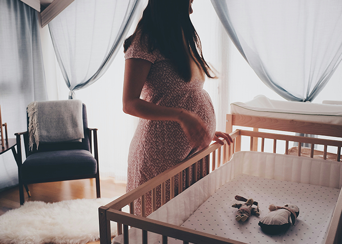 Pregnant woman in a softly lit nursery, standing by a wooden crib, with toys inside, wearing a patterned dress. Pregnant woman in a softly lit nursery, standing by a wooden crib, with toys inside, wearing a patterned dress.