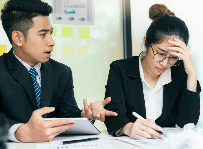 Two frustrated colleagues in a tense meeting, conveying stories about difficult bosses.