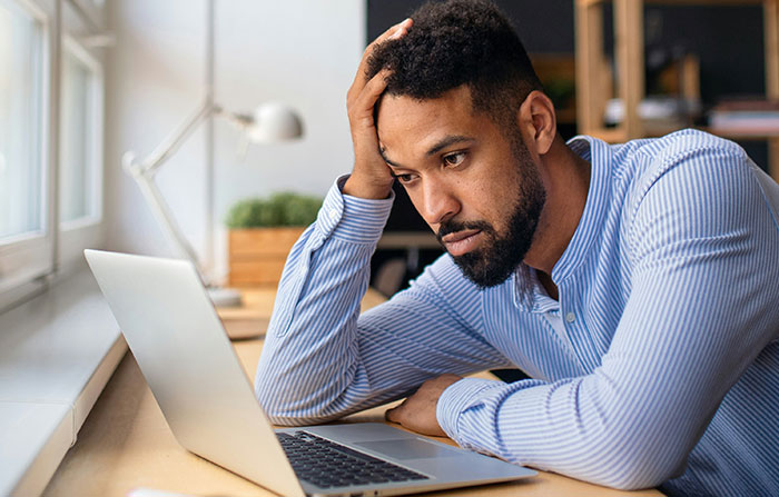 A frustrated employee sits at a desk with a laptop, illustrating stories of difficult bosses.