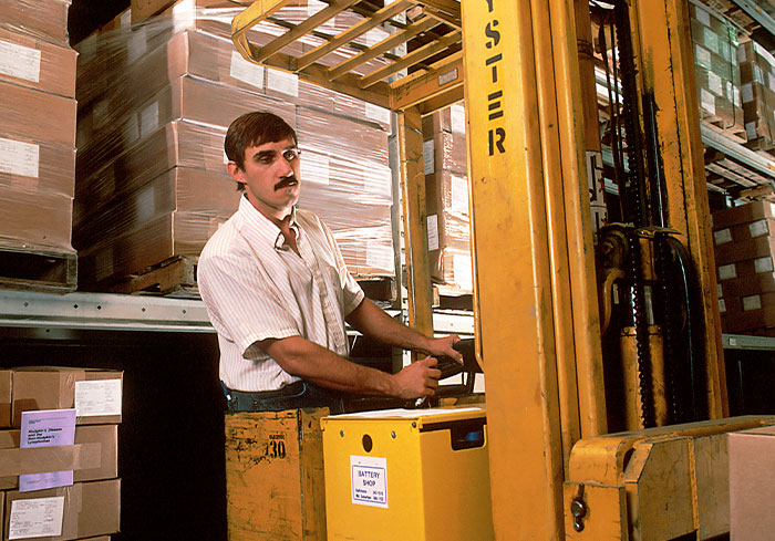 Warehouse worker operating a forklift, surrounded by stacked boxes, highlighting stories about difficult bosses.
