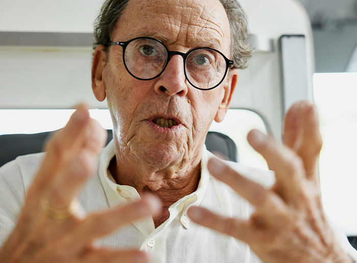 Elderly man in glasses gesturing expressively, possibly sharing a story about a challenging boss.