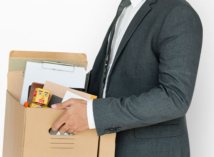 Man in a suit holding a box of personal items, symbolizing stories about bosses from hell.