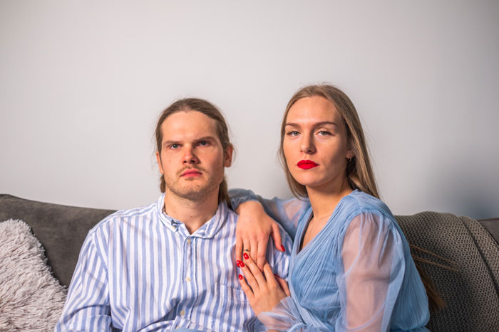 A man and woman sitting on a couch; the man looks flabbergasted. A man and woman sitting on a couch; the man looks flabbergasted.