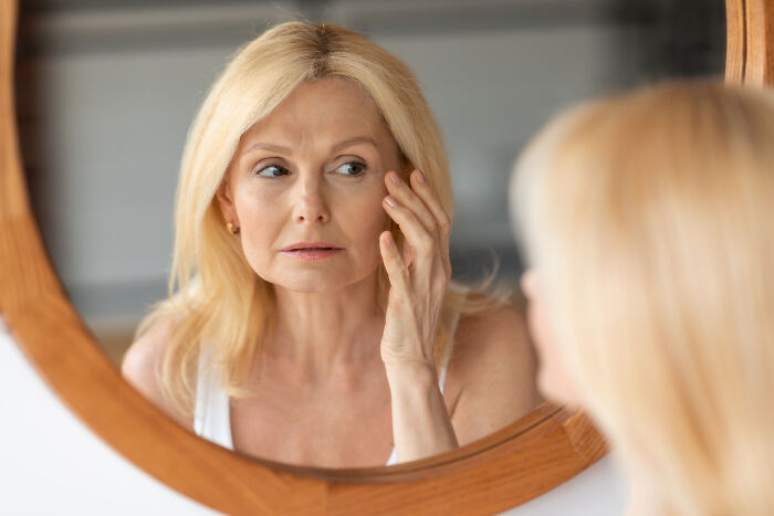 Woman looking concerned at her reflection in mirror, touching face, focusing on an insignificant thing.