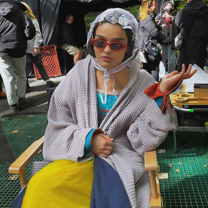 Actress on set in costume for 'Snow White,' wearing sunglasses and a bonnet, sitting casually in a director's chair. Actress on set in costume for 'Snow White,' wearing sunglasses and a bonnet, sitting casually in a director's chair.