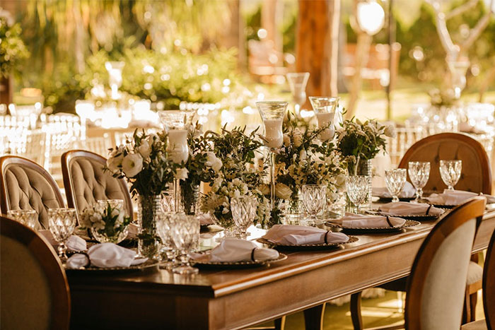 Elegant wedding table setup with floral centerpieces and crystal glassware outdoors. Elegant wedding table setup with floral centerpieces and crystal glassware outdoors.