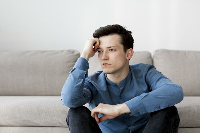 Young man in blue shirt sitting on a couch, pensive expression, related to grandma taking baby away debate. Young man in blue shirt sitting on a couch, pensive expression, related to grandma taking baby away debate.