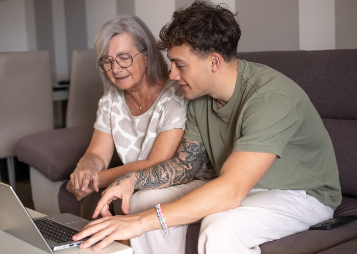 Grandma and young man on a sofa, looking at a laptop together, discussing weekend plans. Grandma and young man on a sofa, looking at a laptop together, discussing weekend plans.