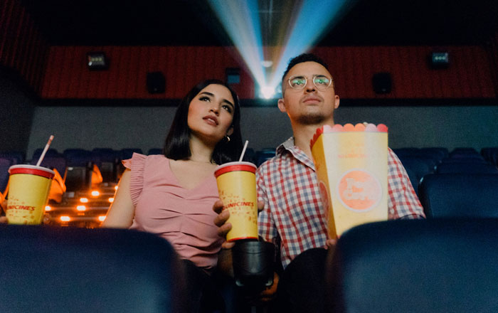 Moviegoers with popcorn and drinks, looking at the screen in a dimly lit theater. Moviegoers with popcorn and drinks, looking at the screen in a dimly lit theater.