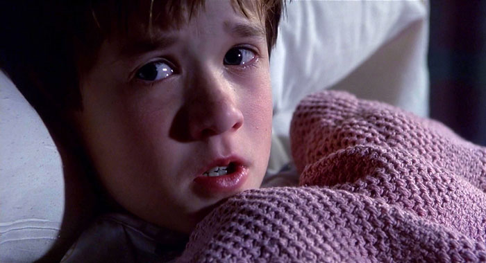 A child looks worried under a pink blanket, eyes wide open in the dim light. A child looks worried under a pink blanket, eyes wide open in the dim light.