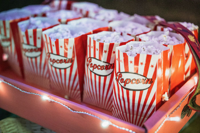 Movie popcorn in red and white striped bags on a pink tray, representing a theater setting. Movie popcorn in red and white striped bags on a pink tray, representing a theater setting.