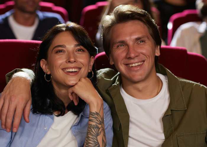 Couple enjoying a movie in a theater, surrounded by red seats, highlighting the main character experience. Couple enjoying a movie in a theater, surrounded by red seats, highlighting the main character experience.