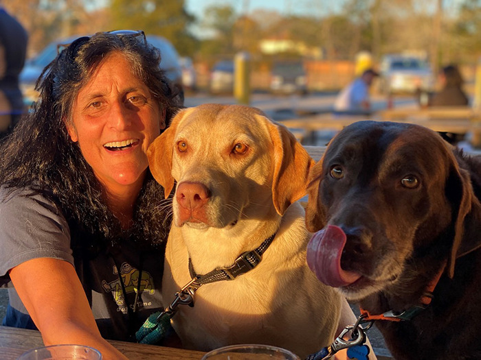 Smiling person with two dogs at an outdoor table, related to NASA astronaut's psychological trauma. Smiling person with two dogs at an outdoor table, related to NASA astronaut's psychological trauma.