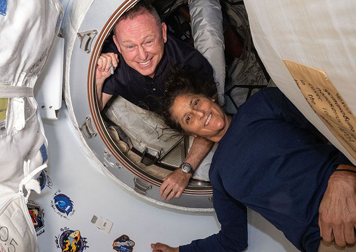 Astronauts smiling inside a space capsule, illustrating effects of long-term space missions on the human body. Astronauts smiling inside a space capsule, illustrating effects of long-term space missions on the human body.